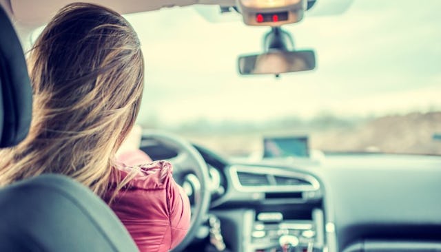 A brunette woman in a burgundy shirt from the back driving her car down a road