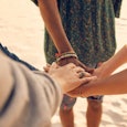 Five young friends holding their hands together while they are standing on the sand who help each ot...