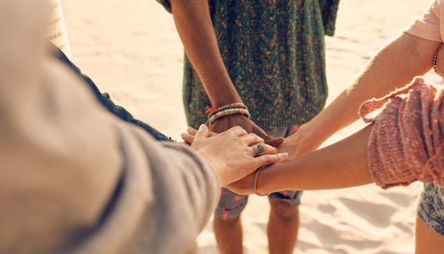 Five young friends holding their hands together while they are standing on a beach and help each oth...