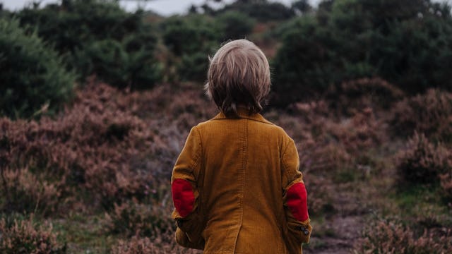 A blonde boy in an orange corduroy jacket with his back turned