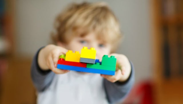 Blonde boy wearing a gray long sleeved shirt while showing what he made from LEGO blocks