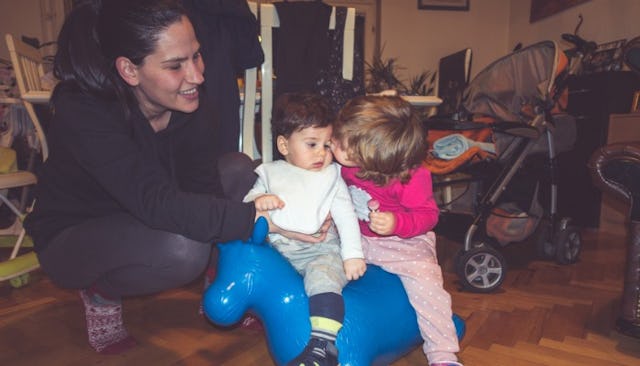 A stay-at-home mom having playtime with her two kids on a blue toy horse in a living room
