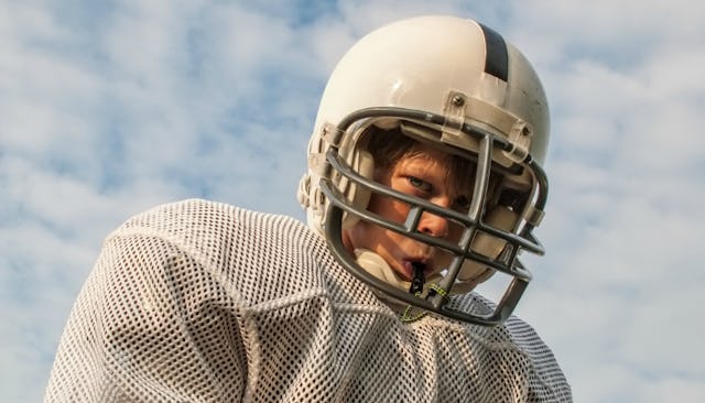 A blonde blue-eyed boy wearing a football shirt and helmet