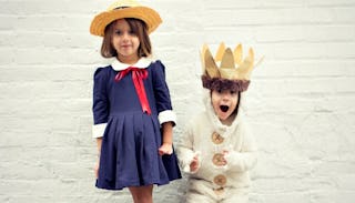 A girl in a navy dress and a small boy in a white king costume