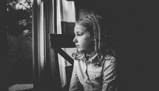 A girl sitting and looking through a window in black and white