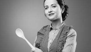 A mother in a polka dot and checkered blouse holding a wooden spoon and smiling in black and white