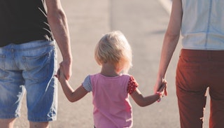 A father in a black shirt and denim shorts, a toddler in a pink shirt, and a mother in a white top a...