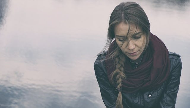 A woman in a black leather jacket and red scarf looking down with a sad facial expression after expe...