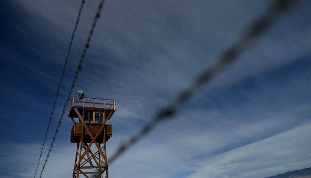 A wooden watch tower behind the barbed wire with a cloudy grey sky