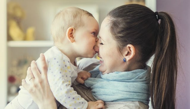 A newborn baby kissing his mother's nose while the mom is holding him and smiling