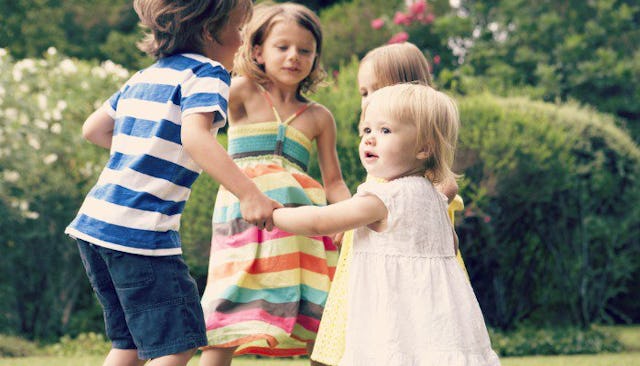 A boy and three girls holding hands and standing in a circle in a garden