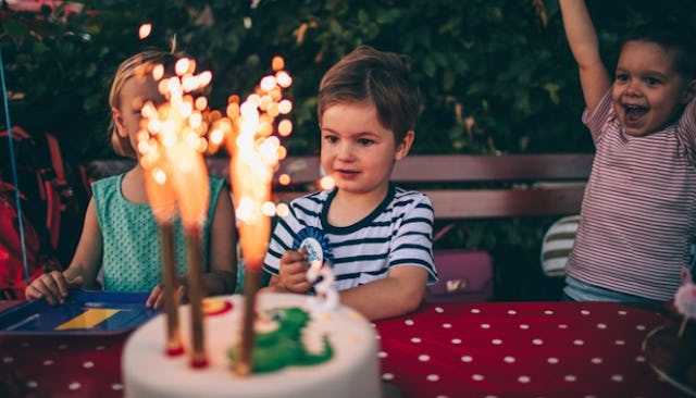 Kids sitting at a picnic table that has a cake with three candles and a dinosaur on it