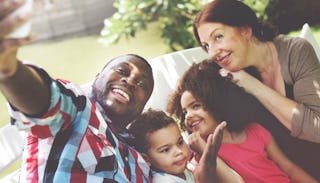 A family of four sitting on a bench and smiling while posing for a selfie.