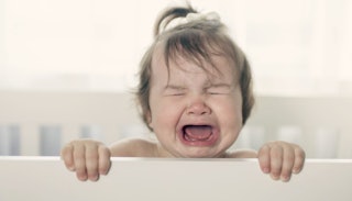 A brown-haired baby crying in a crib 