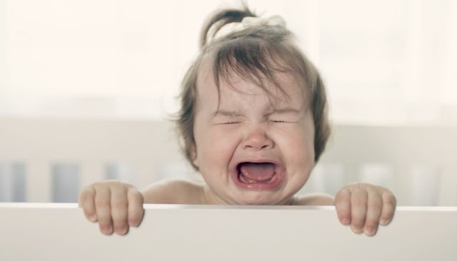 A brown-haired baby crying in a crib