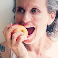 Gray-haired tattooed woman biting an apple.