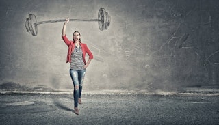 A woman in a red blazer and blue jeans standing and yelling while holding an illustrated dumbbell ab...