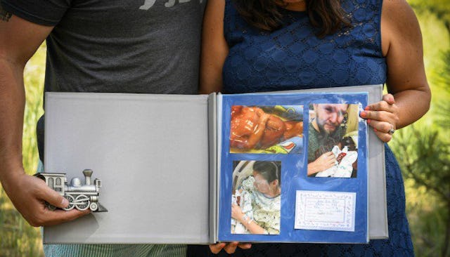 A mother and father holding a photo album with photographs of their stillborn son