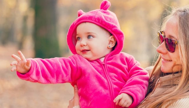 A babysitter holding a baby dressed in a pink hoodie in a park