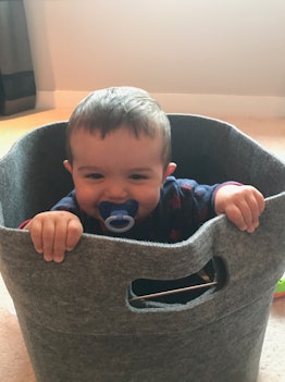 A smiling baby sitting in the laundry basket