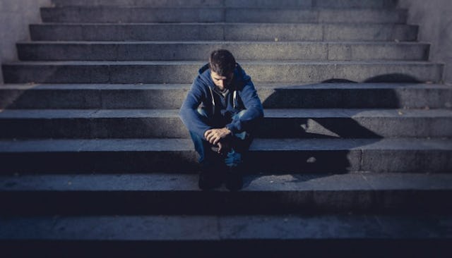 A teen addict sitting on concrete stairs in a blue hoodie and blue denim jeans while looking down