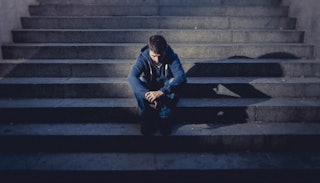 A teen who is an addict sitting on brick stairs and looking down.