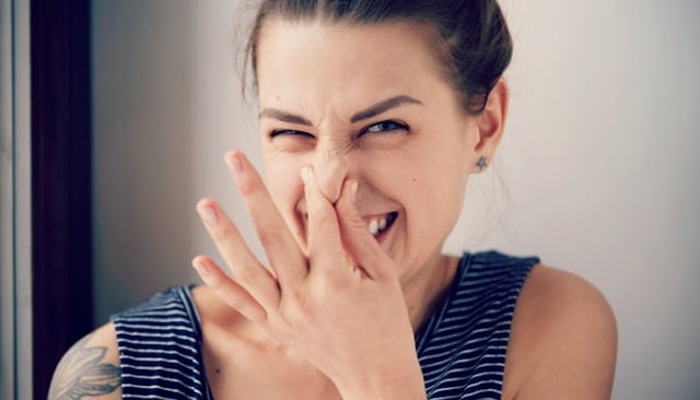Woman wearing a blue striped shirt with a tattoo on her right shoulder smiling and holding her nose ...
