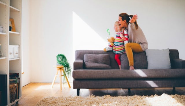 A mother and her daughter sitting on a grey couch in a living groom and playing togehter