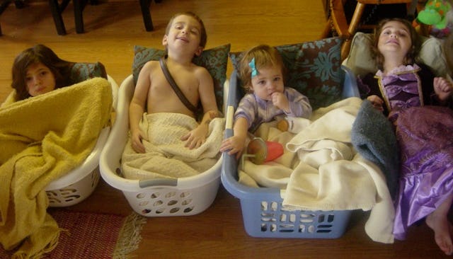 Four children lying in dirty laundry baskets
