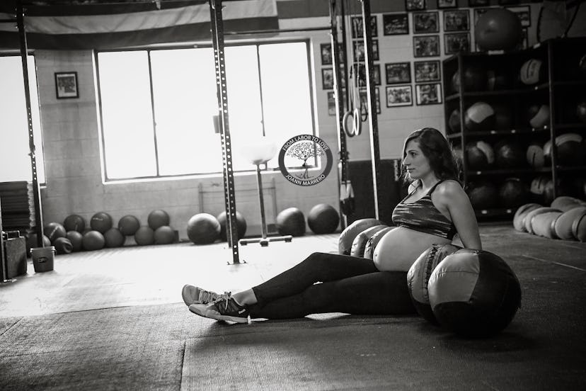 Pregnant fit mom sitting on the floor in the training room with training balls all around her