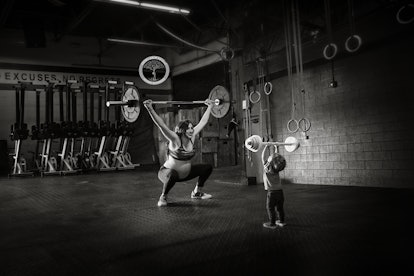 A fit mom happily doing weight exercises with her young child inside the gym