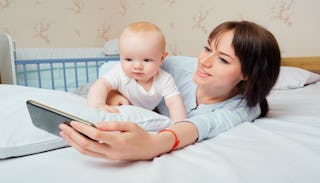 Young mom smiling and taking a selfie with her newborn baby while lying on a bed