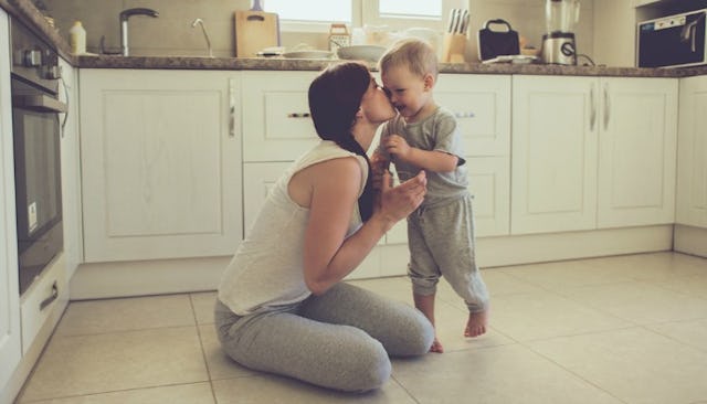 Mom sitting on the floor in the kitchen and kissing her kid 