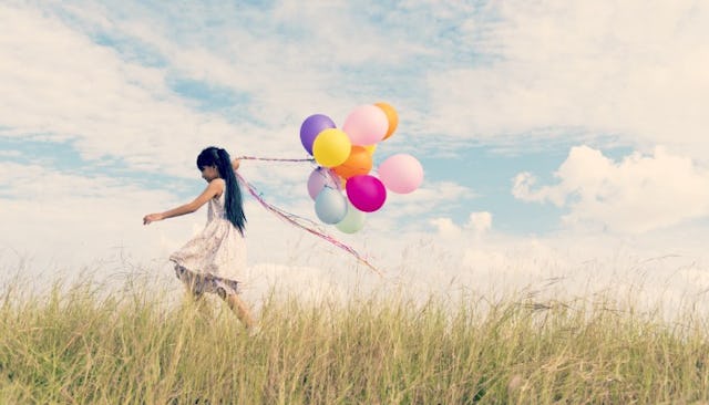 A girl running through a field holding a bunch of balloons