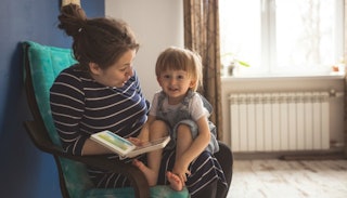 Woman wearing a black dress with white stripes while reading a story to her blonde child in her lap