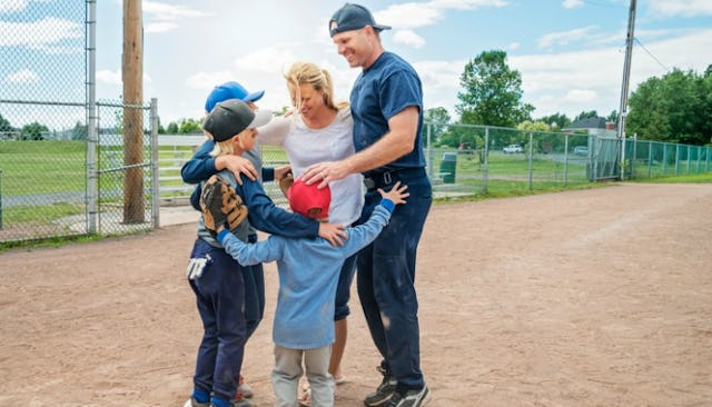 Parents and their three sons in a group hug after a baseball game