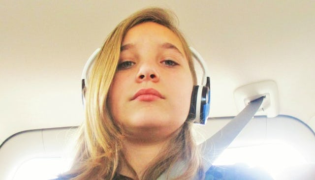 A teenager taking a selfie with her buckled up in the car while wearing a blue shirt and blue and wh...