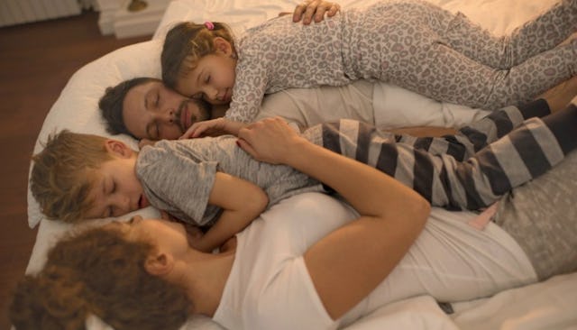 A family of four, a woman, her husband and their two sons lying in bed hugged and sleeping