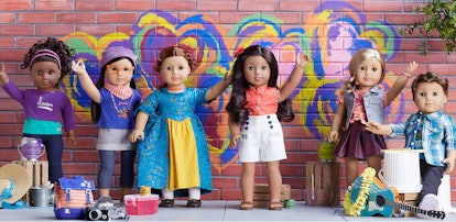 6 American Girl dolls placed together and with one arm raised like they're waving