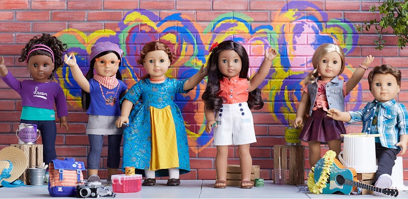 6 American Girl dolls placed together and with one arm raised like they're waving