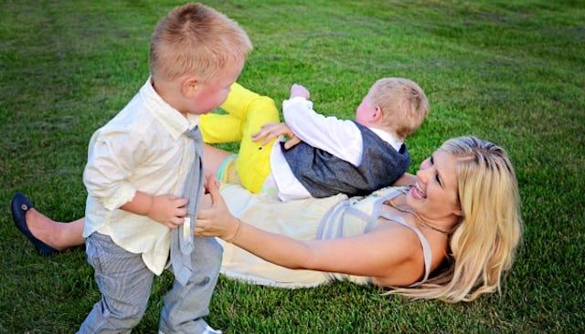 Blonde woman lying on the grass, laughing and playing with her two little sons