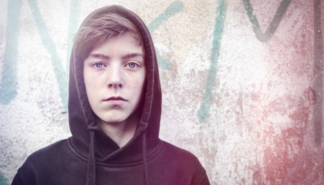 A teen boy with brown hair looking towards the camera while wearing a black hoodie