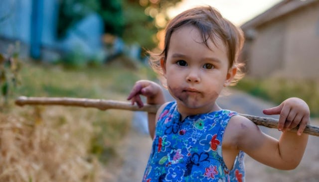A toddler girl with a wild spirit holding a tree branch