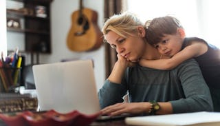 A child hugging his depressed mother looking at her laptop.