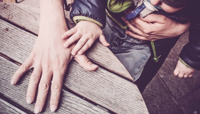 A mother's and a baby's hand on a wooden table.