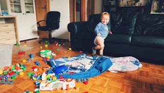 A kid standing next to a lot of toys on the living room floor 