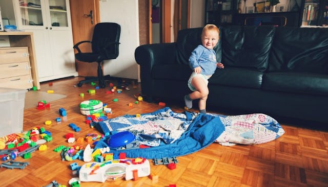 A kid standing next to a lot of toys on the living room floor