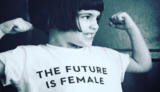 Little girl grinning and flexing her arms with a white shirt saying "the future is female"