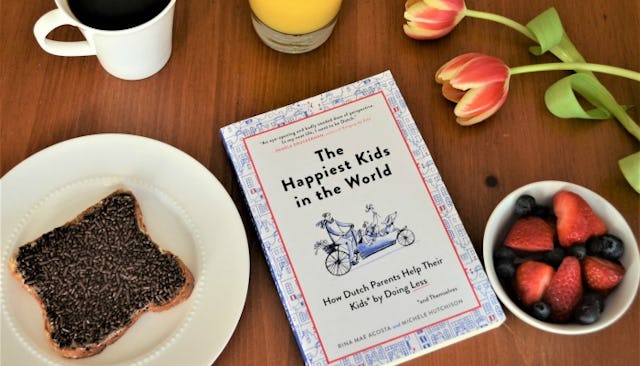 Coffee and toast on a brown table with a book next to them called The happiest kids in the world tha...