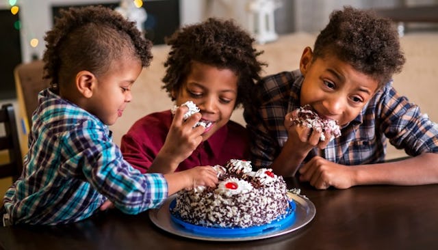 Three Rambunctious boys having fun while eating a cake with their hands